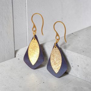 Boucles d'oreilles forme larme en cuir sauvage bleu, taille réduite, finition aniline et pendants dorés brossés, vues de face, suspendues à des boucles dorées sur béton