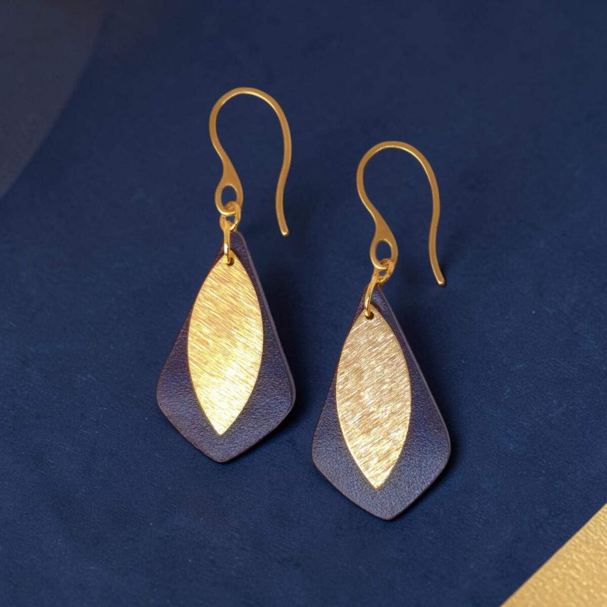Boucles d'oreilles forme larme en cuir sauvage bleu, taille réduite, finition aniline et pendants dorés brossés, vues de face, suspendues à des boucles dorées, fond design