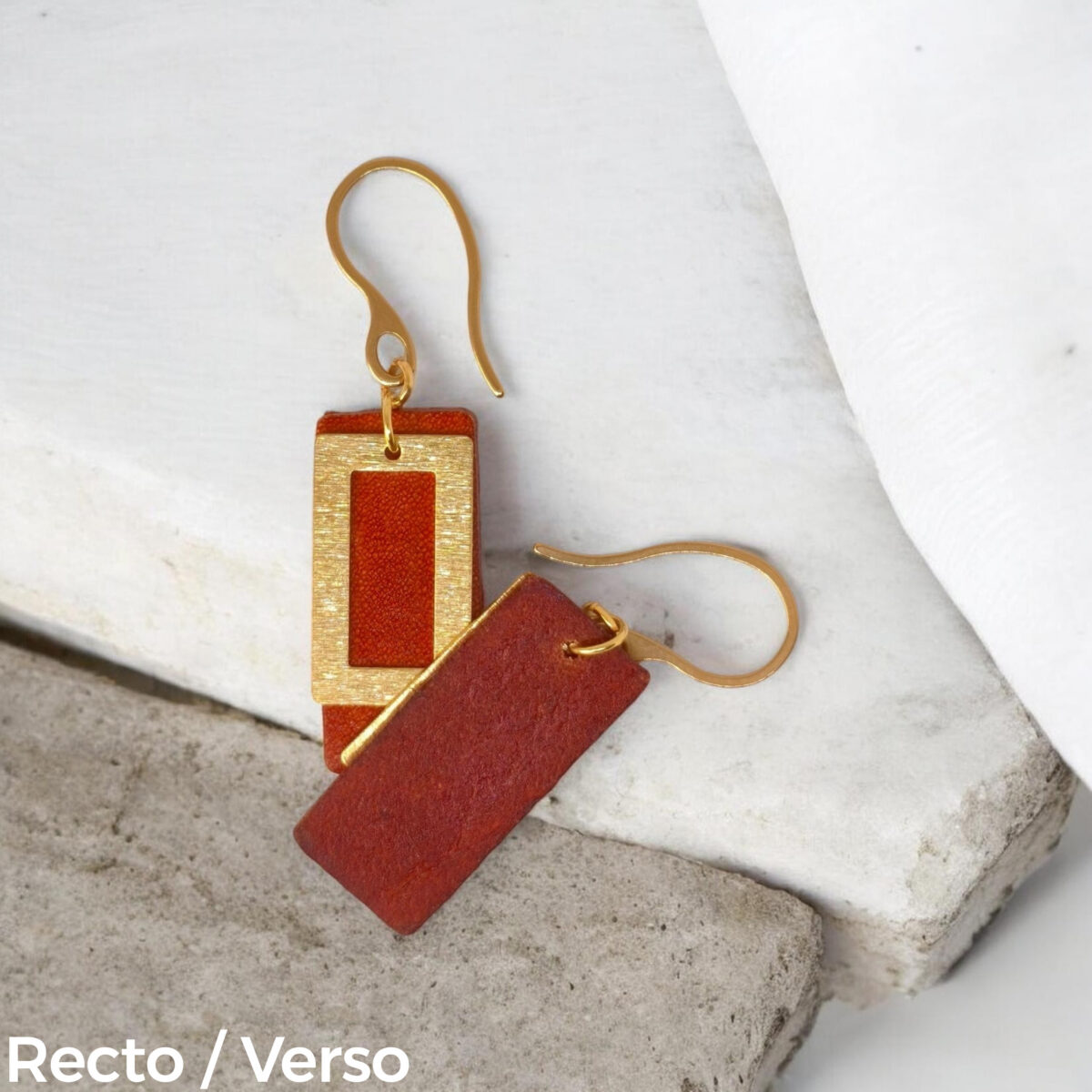 Boucles d'oreilles rectangulaires en cuir teinté cognac, finition lisse et pendant brossé doré, vues recto - verso se chevauchant, suspendues à des boucles dorées, sur pierre