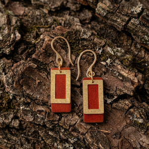 Boucles d'oreilles rectangulaires en cuir teinté cognac, finition lisse et pendant brossé doré, vues de face, suspendues à des boucles dorées, sur écorce