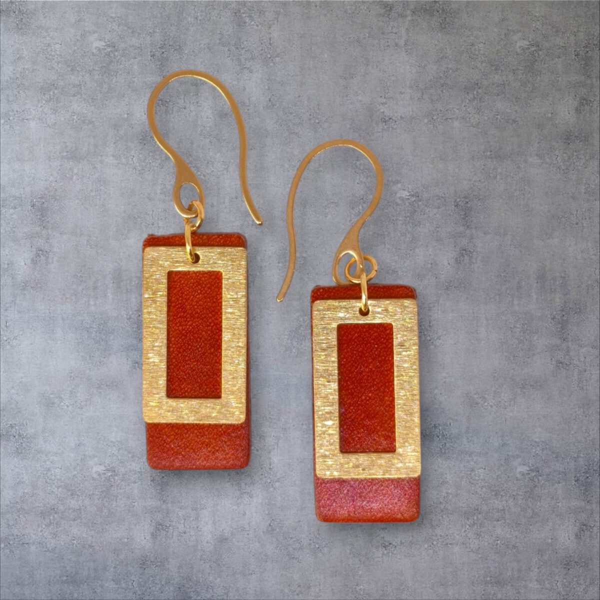 Boucles d'oreilles rectangulaires en cuir teinté cognac, finition lisse et pendant brossé doré, vues de face, suspendues à des boucles dorées, fond gris