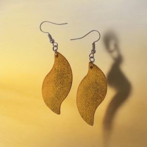 Boucles d'oreilles forme feuille asymétrique en cuir teinté jaune, texturage lime fine vieillie, vues de face, suspendues à des boucles gun métal, fond jaune