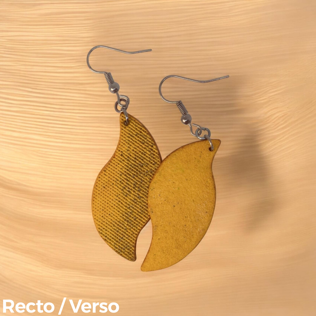 Boucles d'oreilles forme feuille asymétrique en cuir teinté jaune, texturage lime fine vieillie, vues recto - verso se chevauchant, suspendues à des boucles gun métal, fond sable