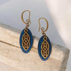 Boucles d'oreilles ovales en cuir teinté bleu, finition lisse et pendant celtique, vues de face, suspendues à des boucles couleur bronze, sur pierre