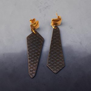 Boucles d'oreilles asymétriques formes cravates en cuir teinte noir charbon, texturage poisson fin, vues de face, suspendues à des apprêts carrés dorés, fond design