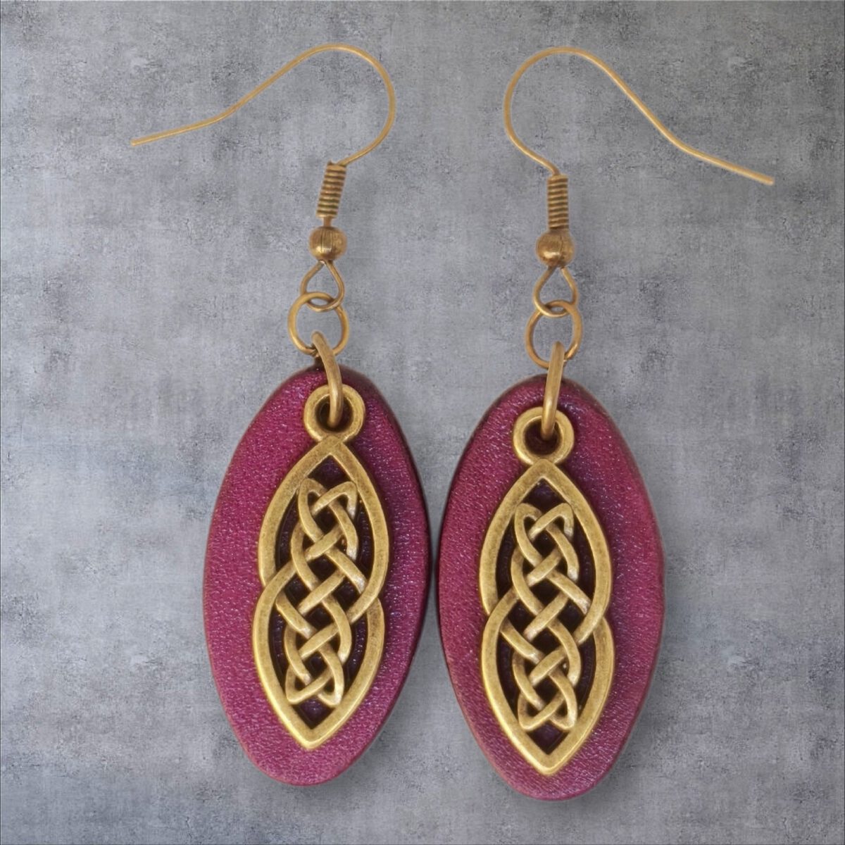 Boucles d'oreilles ovales en cuir teinté violet, finition lisse et pendant celtique, vues de face, suspendues à des boucles couleur bronze sur fond gris