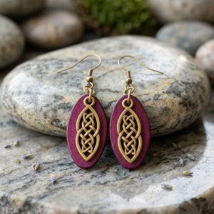 Boucles d'oreilles ovales en cuir teinté violet, finition lisse et pendant celtique, vues de face, suspendues à des boucles couleur bronze sur pierre