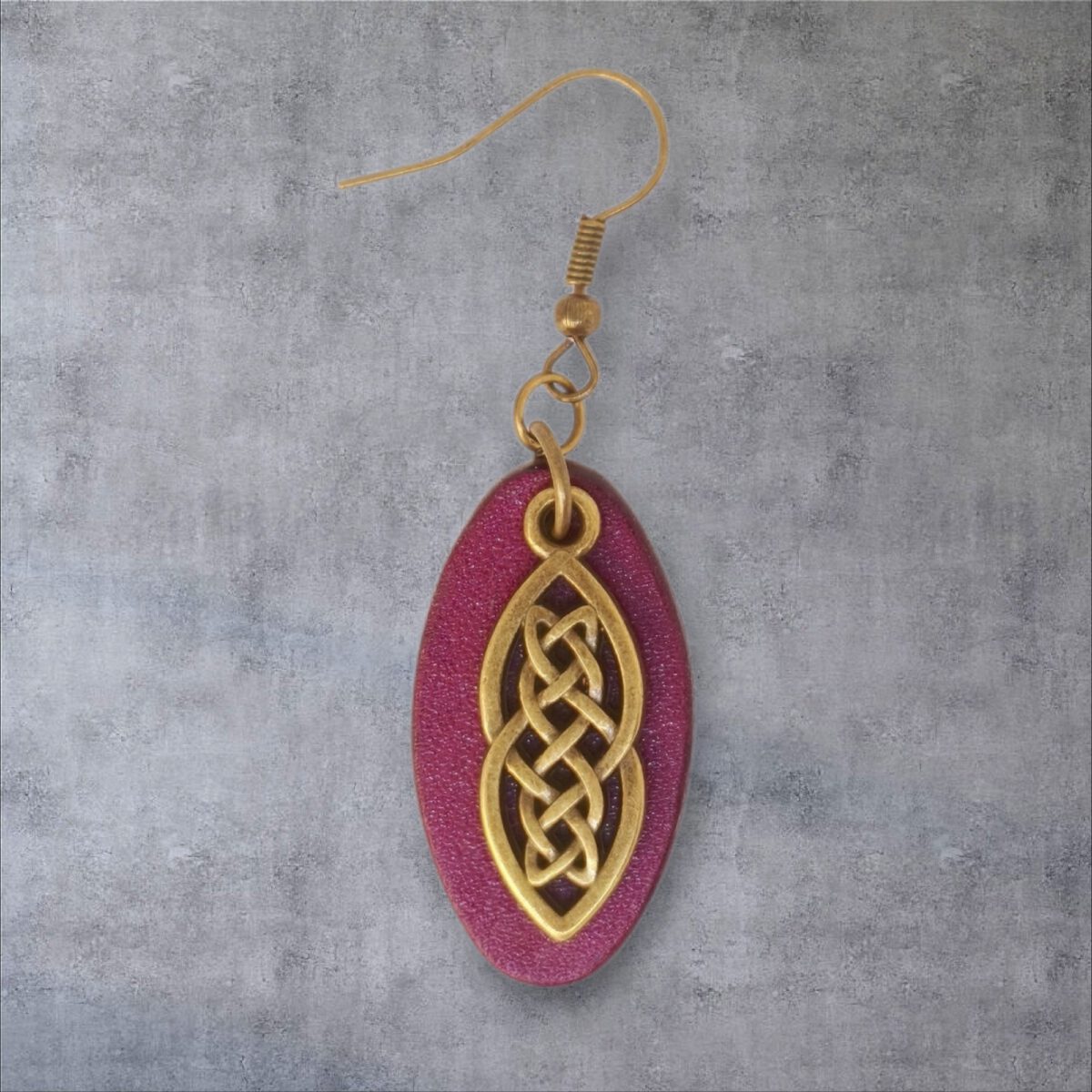 Boucle d'oreille ovale en cuir teinté violet, finition lisse et pendant celtique, vue de face, suspendue à une boucle couleur bronze, fond gris