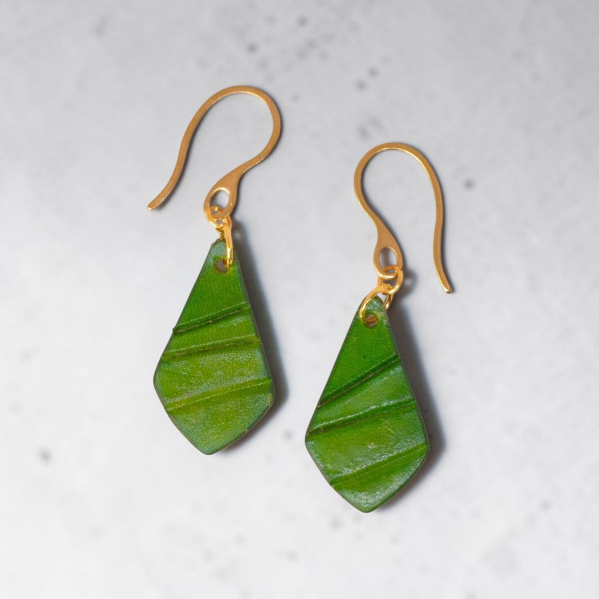 Boucles d'oreilles forme larme en cuir teinture vert forêt, taille réduite, finition galet, vues de face, suspendues à des boucles dorées sur fond gris