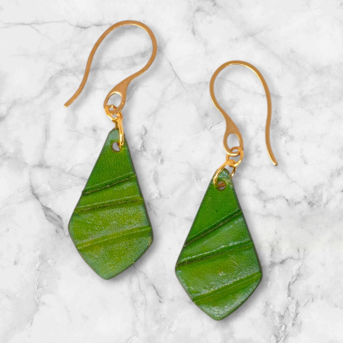 Boucles d'oreilles forme larme en cuir teinture vert forêt, taille réduite, finition galet, vues de face, suspendues à des boucles dorées sur marbre