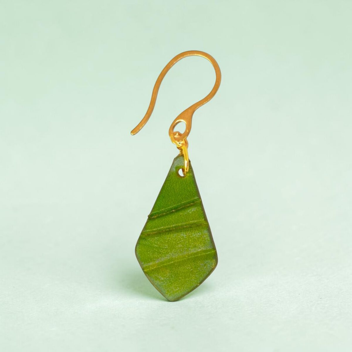Boucle d'oreille forme larme en cuir teinture vert forêt, taille réduite, finition galet, vue de face, suspendue à une boucle dorée, fond design