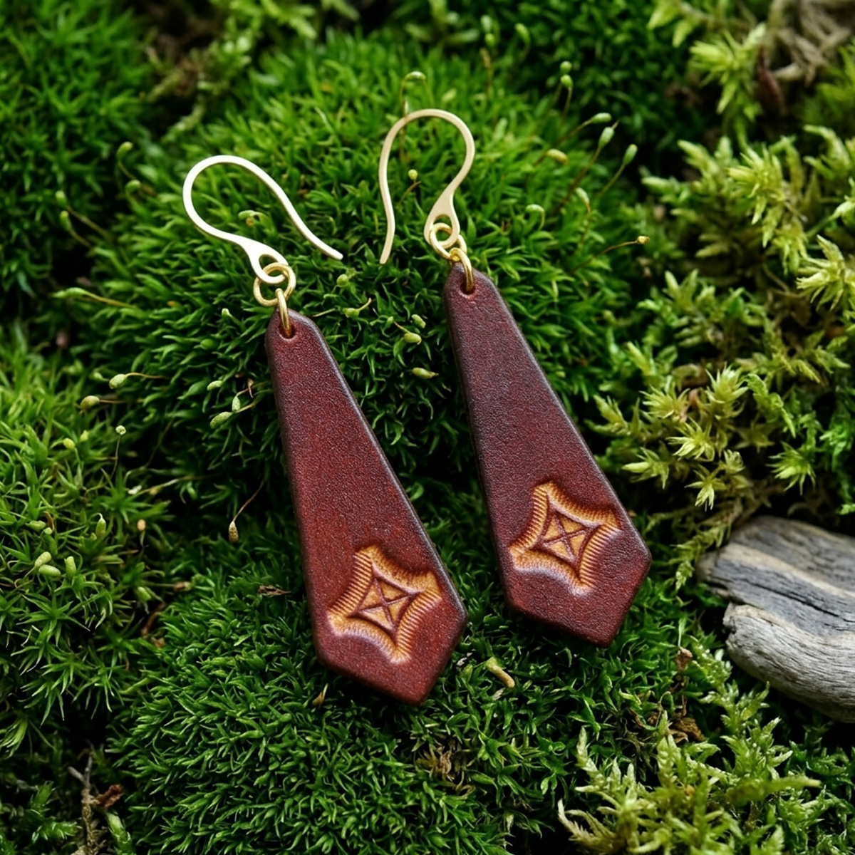Boucles d'oreilles cravates en cuir teinte cognac, estampage croix teintée jaune, vues de face, suspendues à des boucles dorées sur mousse