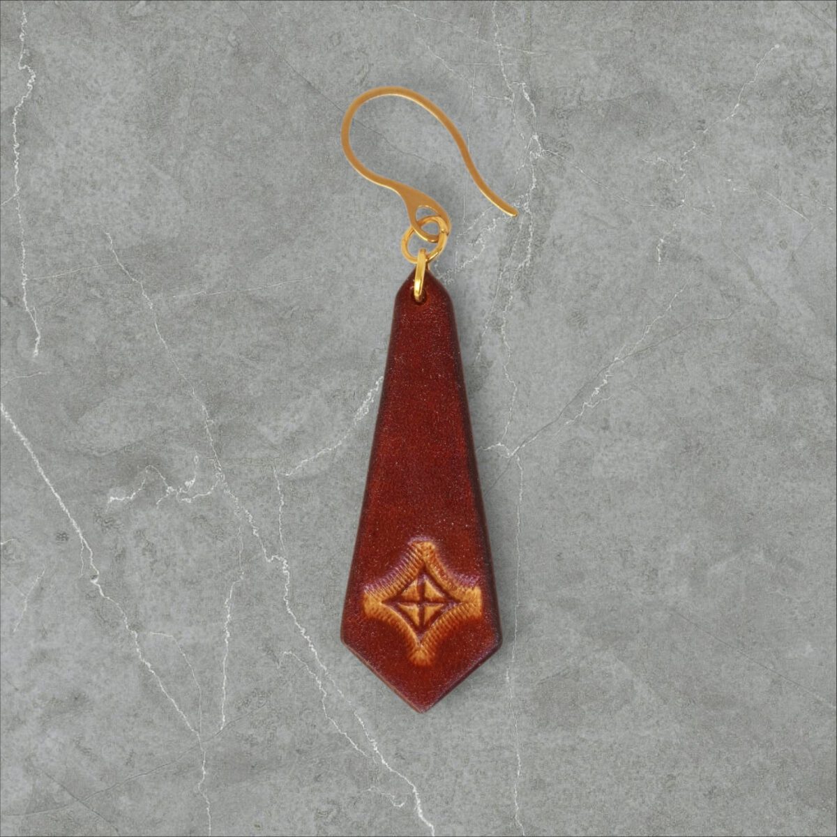 Boucle d'oreille cravate en cuir teinte cognac, estampage croix teintée jaune, vue de face, suspendue à une boucle dorée, fond gris