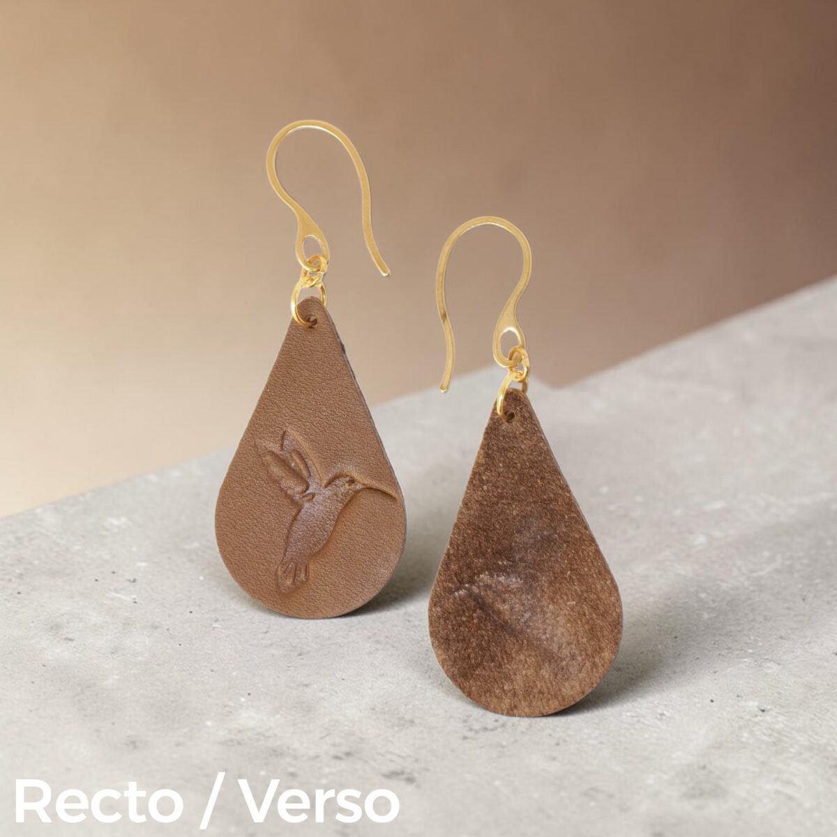 Boucles d'oreilles forme goutte d'eau en cuir marron, estampages colibri, vues recto - verso, suspendues à des boucles dorées sur béton