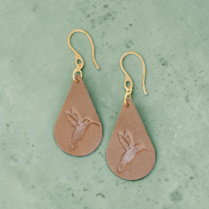 Boucles d'oreilles forme goutte d'eau en cuir marron, estampages colibri, vues de face, suspendues à des boucles dorées sur béton vert