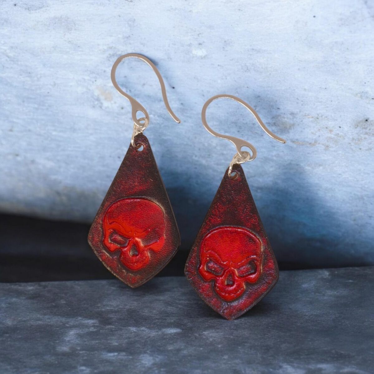 Boucles d'oreilles forme larme en cuir teinture rouge et noire, estampage tête de mort, vues de face, suspendues à des boucles argentées, fond design