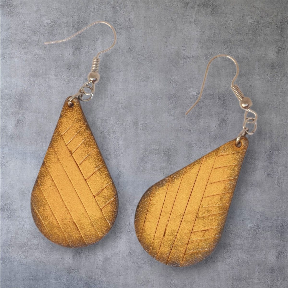 Boucles d'oreilles forme goutte d'eau en cuir teinture jaune dégradée, finition griffée, vues de face, suspendues à des boucles argentées sur fond gris