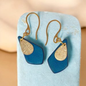 Boucles d'oreilles forme larme en cuir teinture bleue, finition lisse et pendants dorés brossés, vues de face, suspendues à des boucles dorées sur fond design