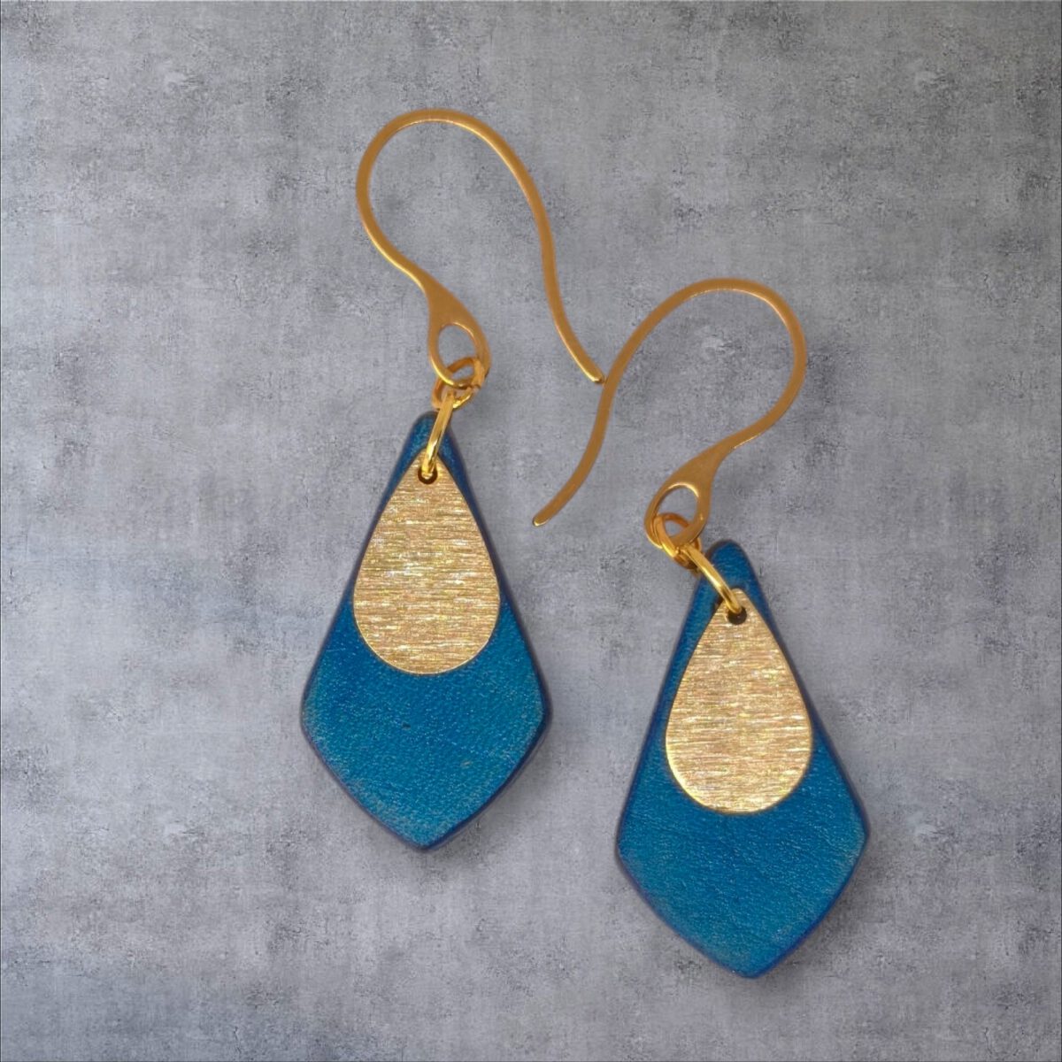 Boucles d'oreilles forme larme en cuir teinture bleue, finition lisse et pendants dorés brossés, vues de face, suspendues à des boucles dorées sur fond gris