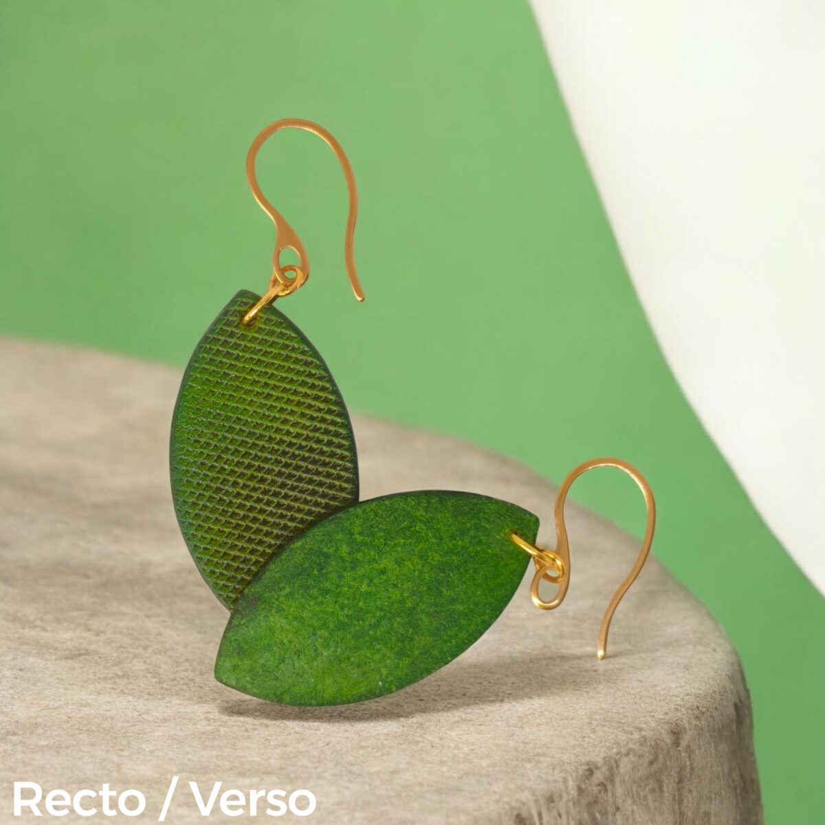 Boucles d'oreilles forme poisson en cuir teinture vert forêt, texturage lime épaisse, vues recto - verso se chevauchant, suspendues à des boucles dorées sur pierre
