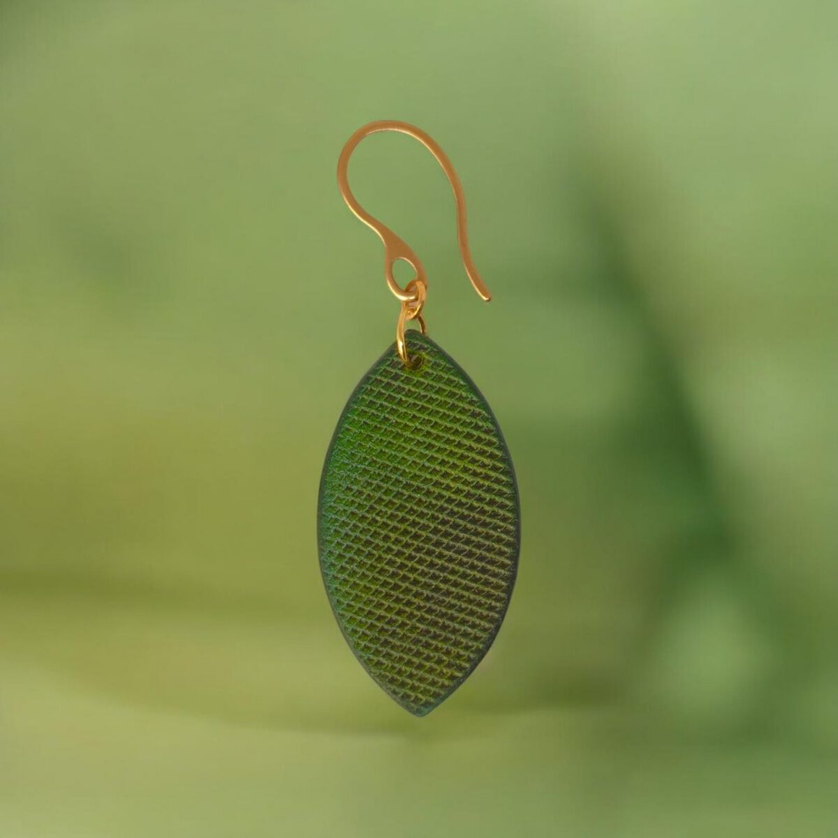 Boucle d'oreille forme poisson en cuir teinture vert forêt, texturage lime épaisse, vue de face, suspendue à une boucle dorée, fond design