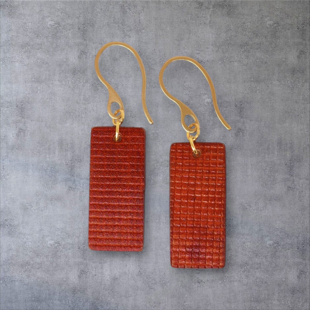 Boucles d'oreilles rectangulaires en cuir teinté cognac, texturage quadrillé, vues de face, suspendues à des boucles dorées, sur fond gris