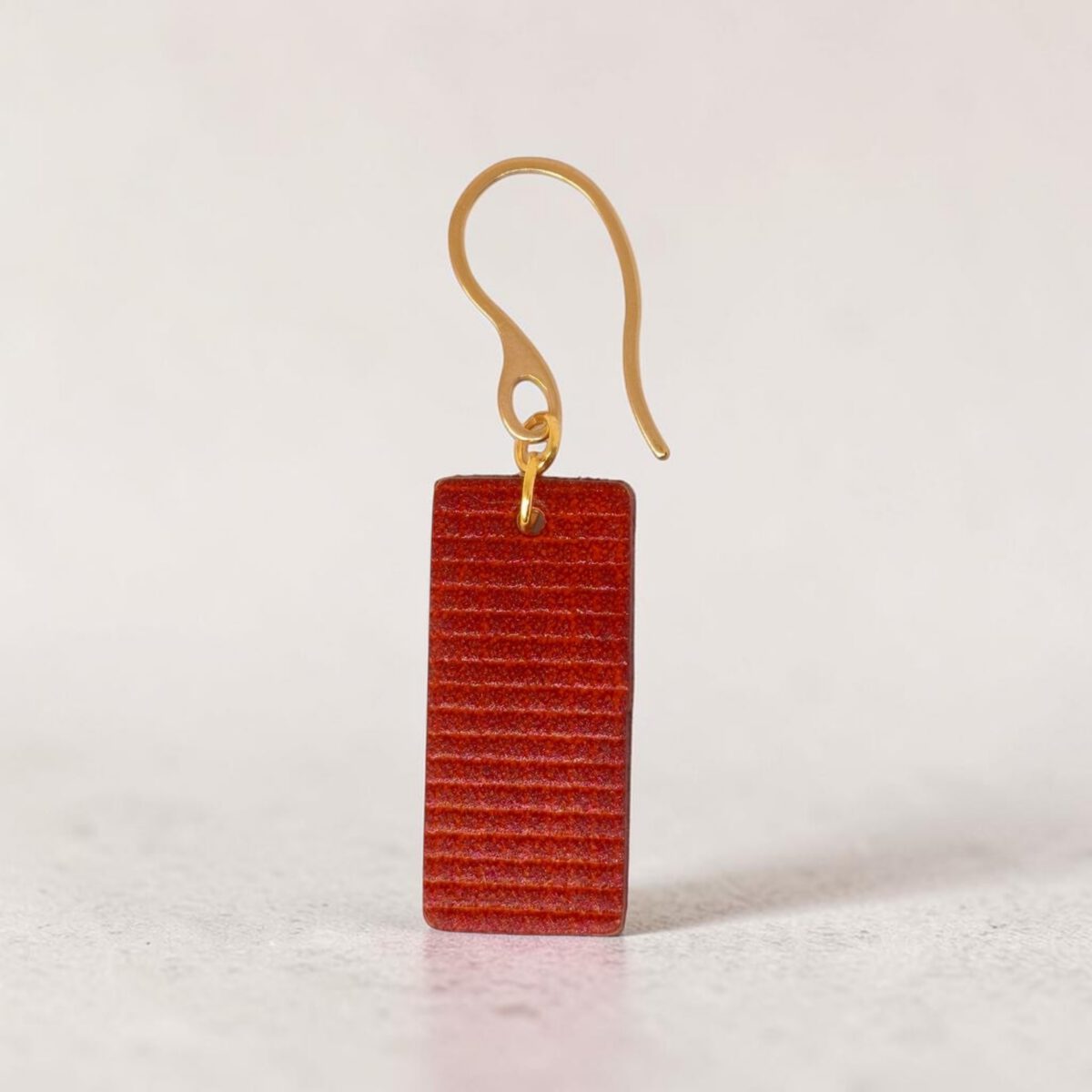 Boucle d'oreille rectangulaire en cuir teinté cognac, texturage quadrillé, vue de face, suspendue à une boucle dorée, fond design