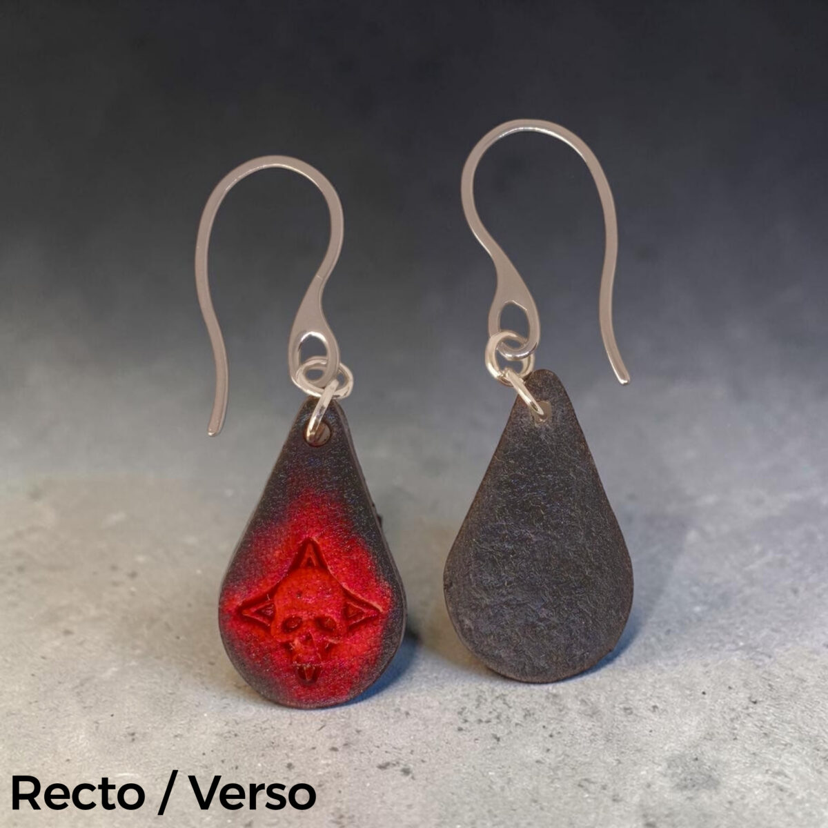 Boucles d'oreilles forme goutte d'eau en cuir teinture noire, estampages tête de mort teintés en rouge, vues recto - verso, suspendues à des boucles argentées