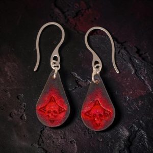 Boucles d'oreilles forme goutte d'eau en cuir teinture noire, estampages tête de mort teintés en rouge, vues de face, suspendues à des boucles argentées sur fond noir
