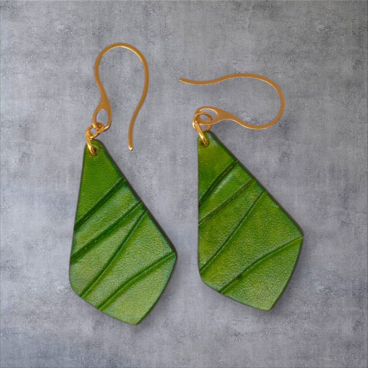 Boucles d'oreilles forme larme en cuir teinture vert forêt, finition galet, vues de face, suspendues à des boucles dorées sur fond gris