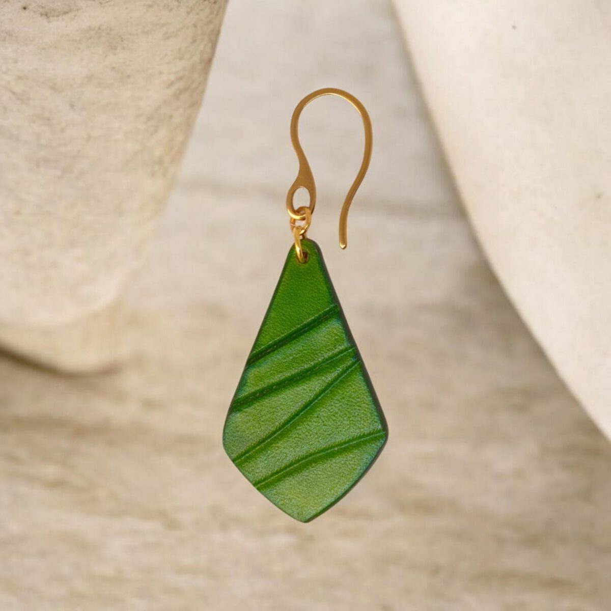 Boucle d'oreille forme larme en cuir teinture vert forêt, finition galet, vue de face, suspendue à une boucle dorée, fond design