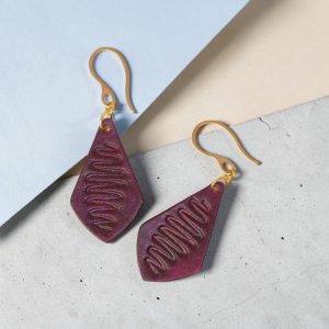 Boucles d'oreilles forme larme en cuir teinture violette, estampage "Lombard Street", vues de face, suspendues à des boucles dorées sur béton