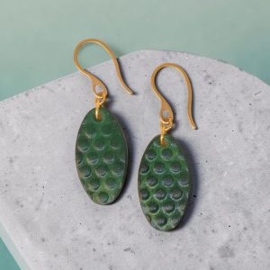 Boucles d'oreilles ovales en cuir teinte vert forêt, texturage ronds, vues de face, suspendues à des boucles dorées sur béton
