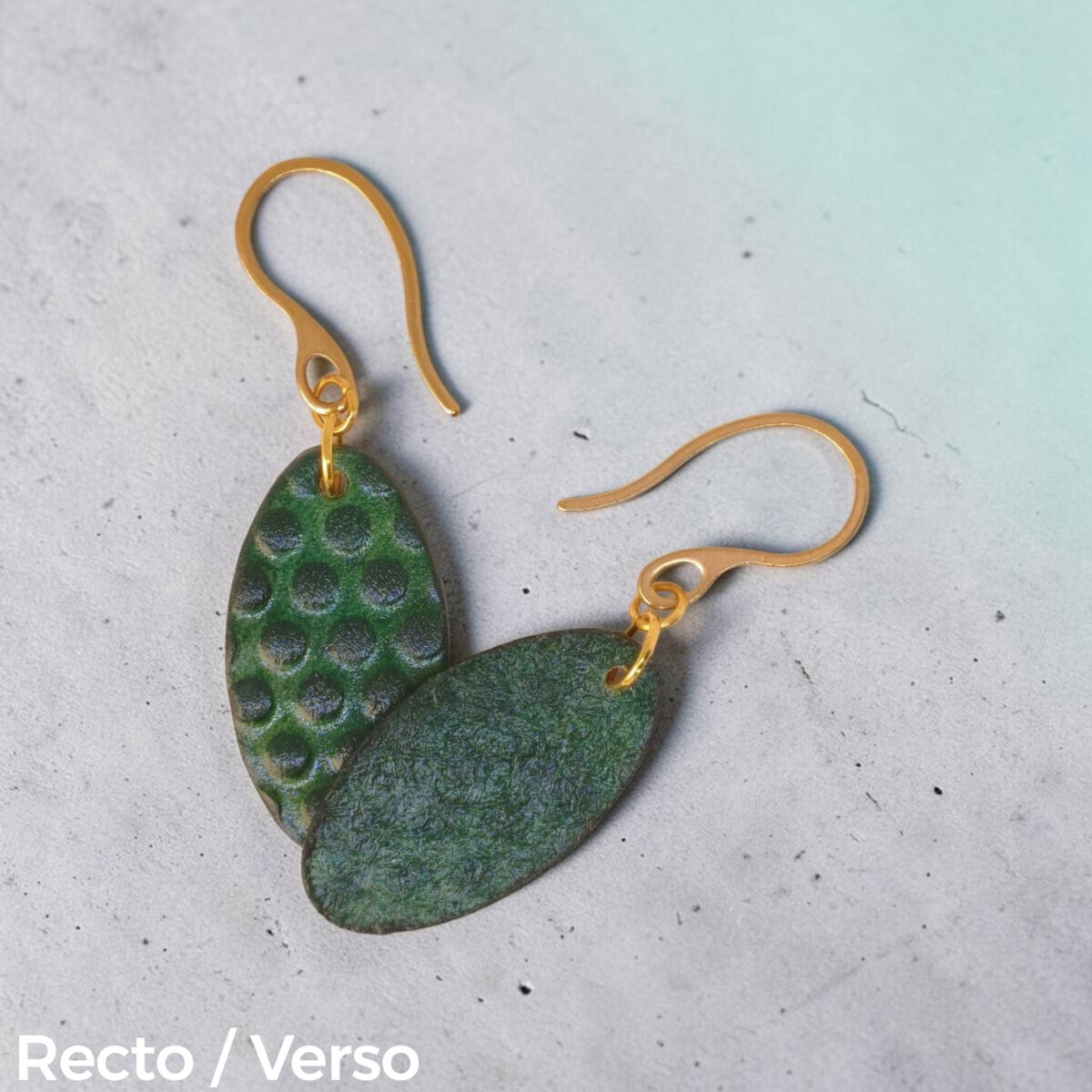 Boucles d'oreilles ovales en cuir teinte vert forêt, texturage ronds, vues recto - verso se chevauchant, suspendues à des boucles dorées sur béton