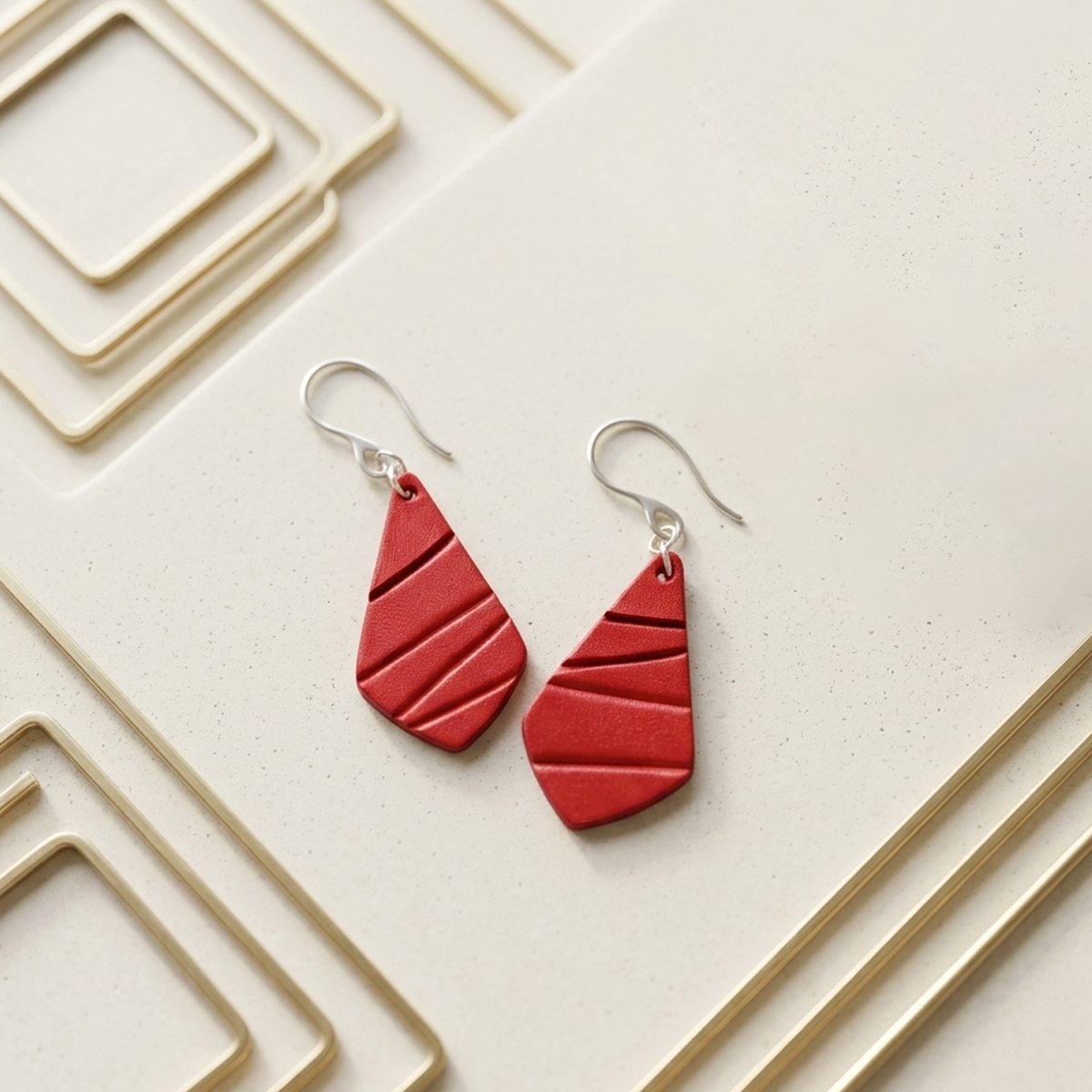 Boucles d'oreilles forme larme en cuir teinture rouge écarlate, finition galet, vues de face, suspendues à des boucles argentées sur fond design