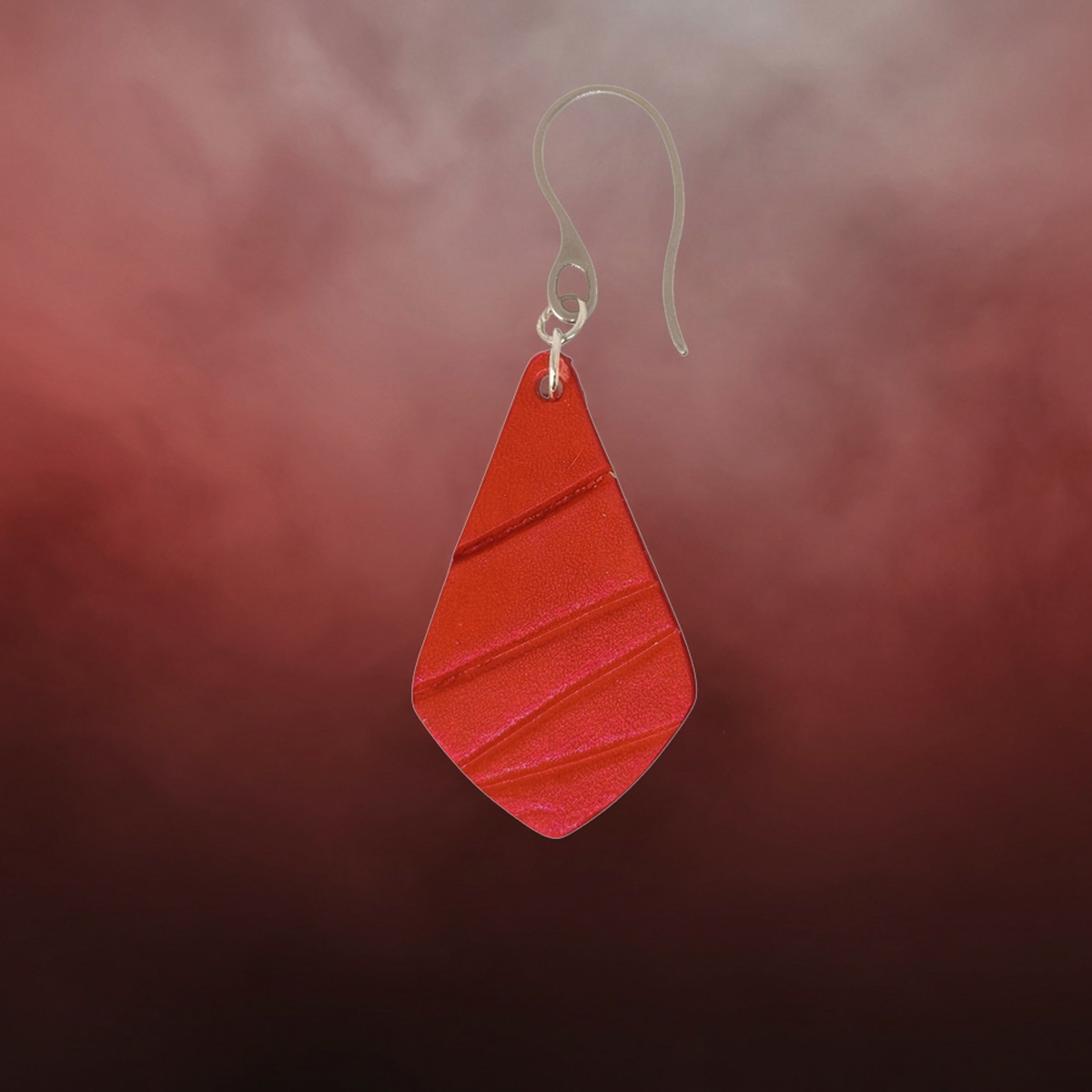 Boucle d'oreille forme larme en cuir teinture rouge écarlate, finition galet, vue de face, suspendue à une boucle argentée, fond design