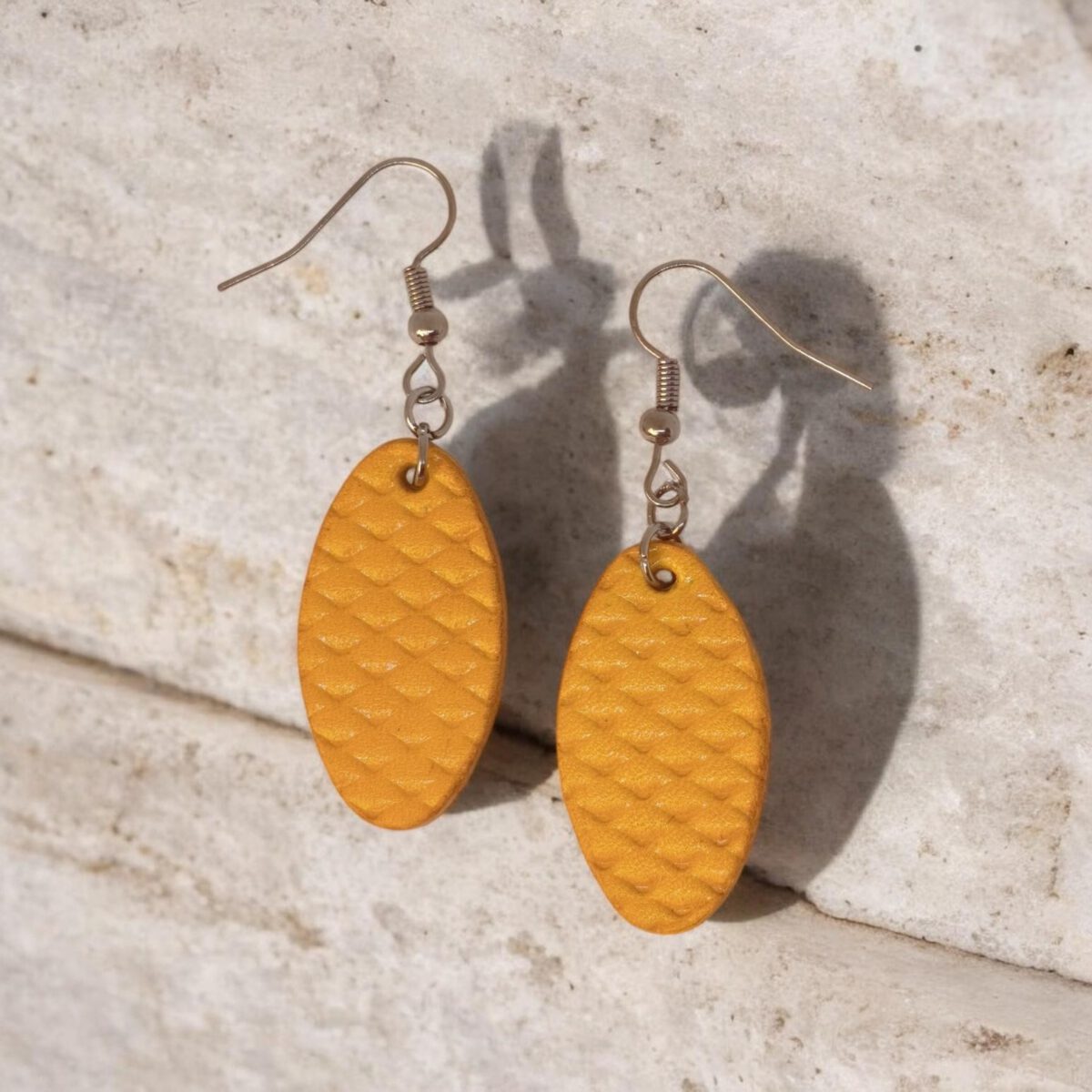 Boucles d'oreilles ovales en cuir teinte jaune, texturage poisson fin, vues de face, suspendues à des boucles argentées sur pierre