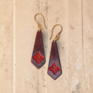 Boucles d'oreilles en cuir teinte acajou, estampage croix teinte rouge, vues de face, suspendues à des boucles dorées fond clair