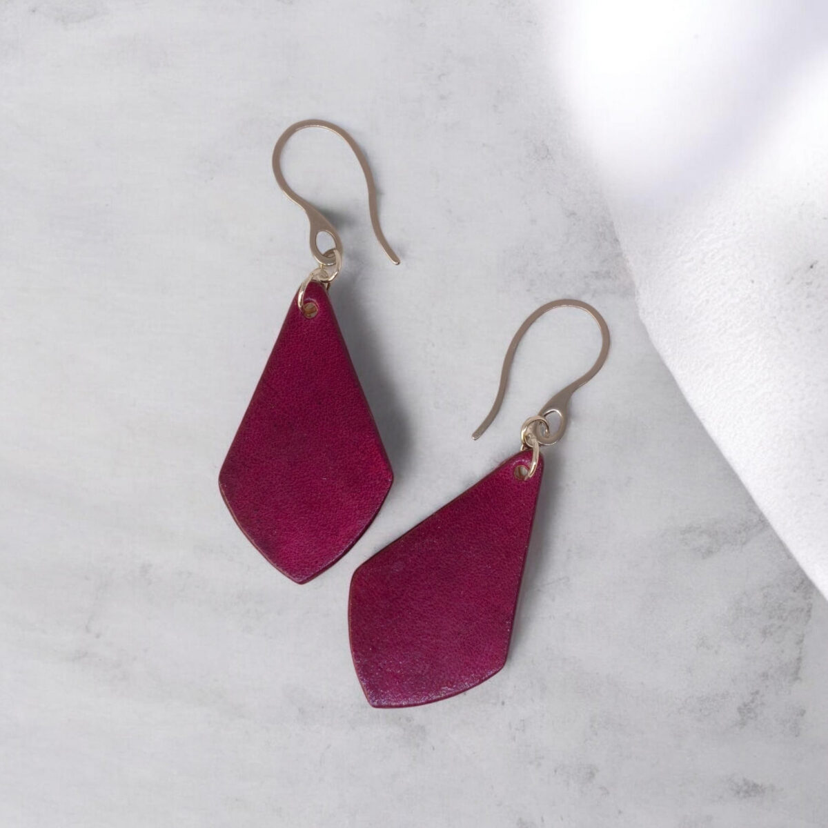 Boucles d'oreilles forme larme en cuir teinture violette, finition lisse, vues de face, suspendues à des boucles argentées sur fond gris clair