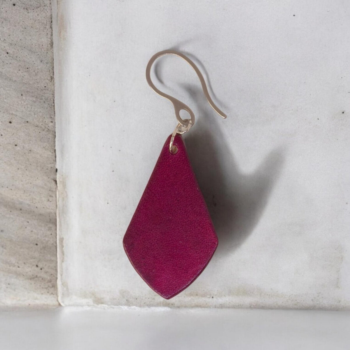 Boucle d'oreille forme larme en cuir teinture violette, finition lisse, vue de face, suspendue à une boucle argentée, sur pierre