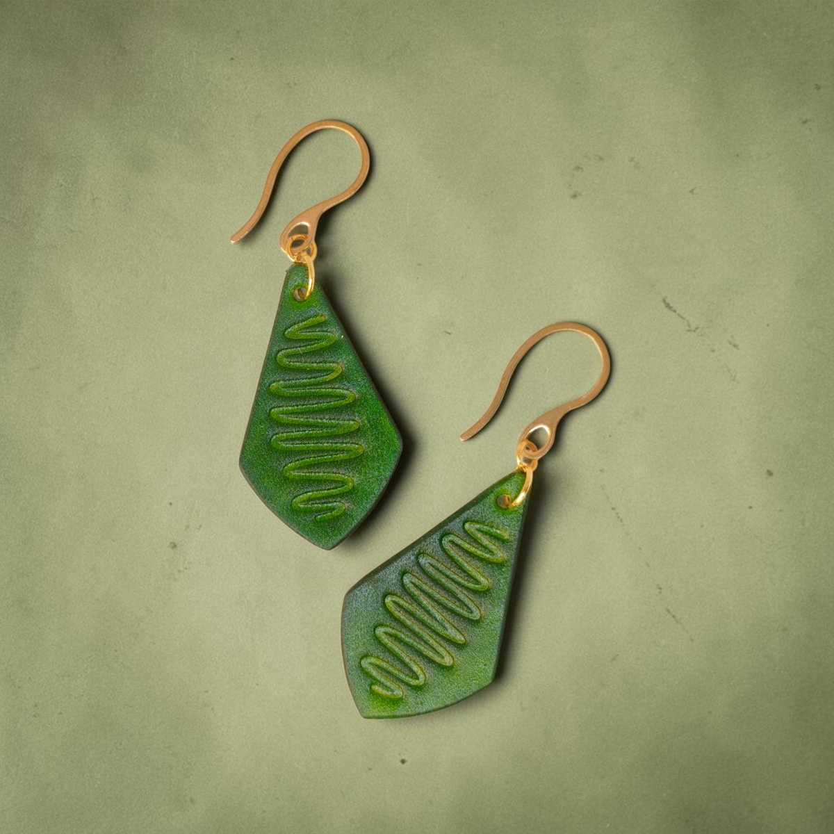 Boucles d'oreilles forme larme en cuir teinture vert forêt, estampage "Lombard Street", vues de face, suspendues à des boucles dorées sur fond vert dégradé
