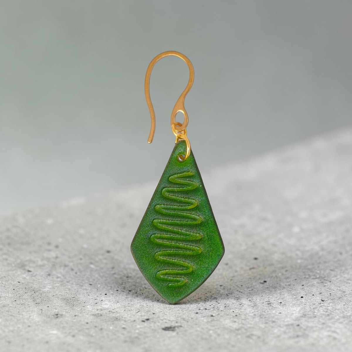 Boucle d'oreille forme larme en cuir teinture vert forêt, estampage "Lombard Street", vue de face, suspendue à une boucle dorée sur béton