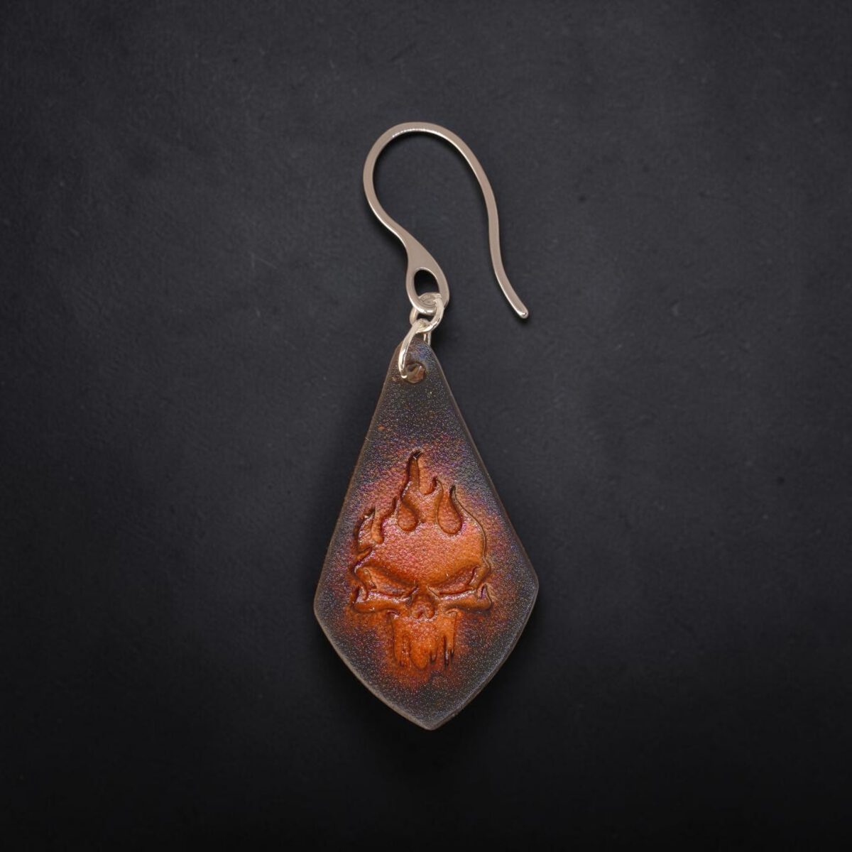 Boucle d'oreille forme larme en cuir teinture noire, estampage tête de mort couleur cognac en dégradé, vue de face, suspendue à une boucle argentée, fond noir