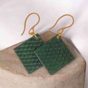 Boucles d'oreilles carrées en cuir teinté vert foncé, texturage poisson, vues de face se chevauchant, suspendues à des boucles dorées sur pierre