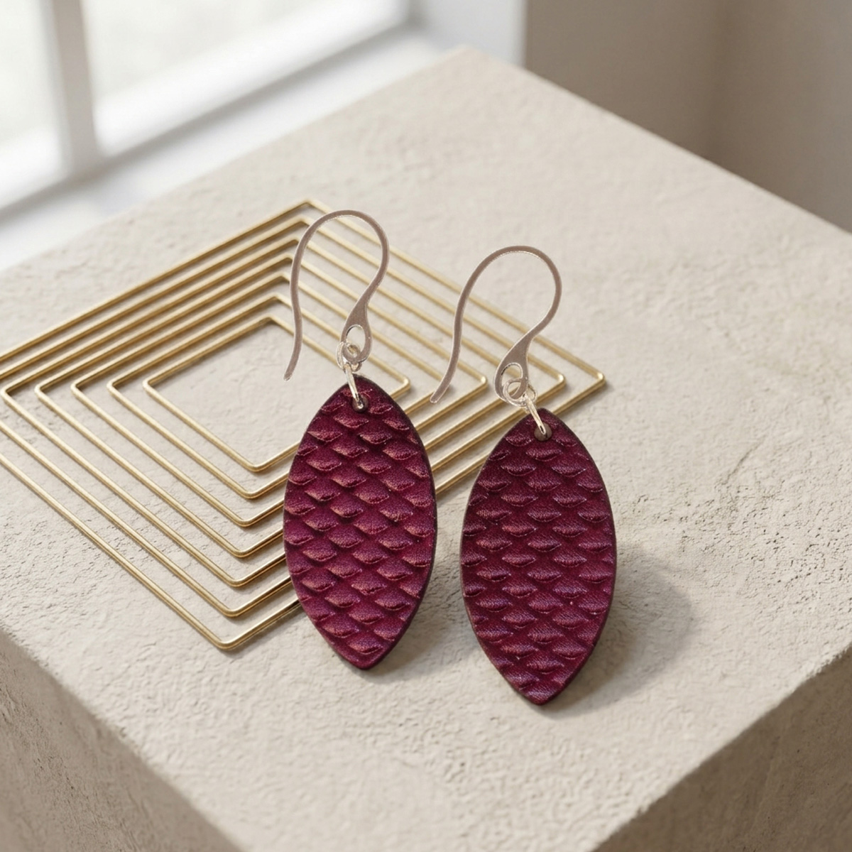 Boucles d'oreilles forme poisson en cuir teinture violet, texturage poisson fin, vues de face, suspendues à des boucles argentées sur fond design