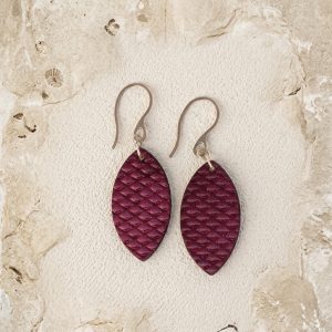 Boucles d'oreilles forme poisson en cuir teinture violet, texturage poisson fin, vues de face, suspendues à des boucles argentées sur sable