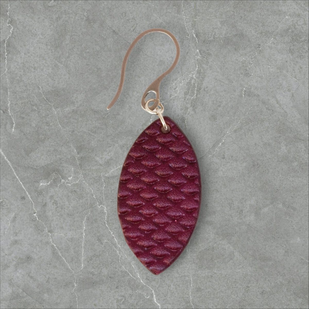 Boucle d'oreille forme poisson en cuir teinture violet, texturage poisson fin, vue de face, suspendue à une boucle argentée, fond gris