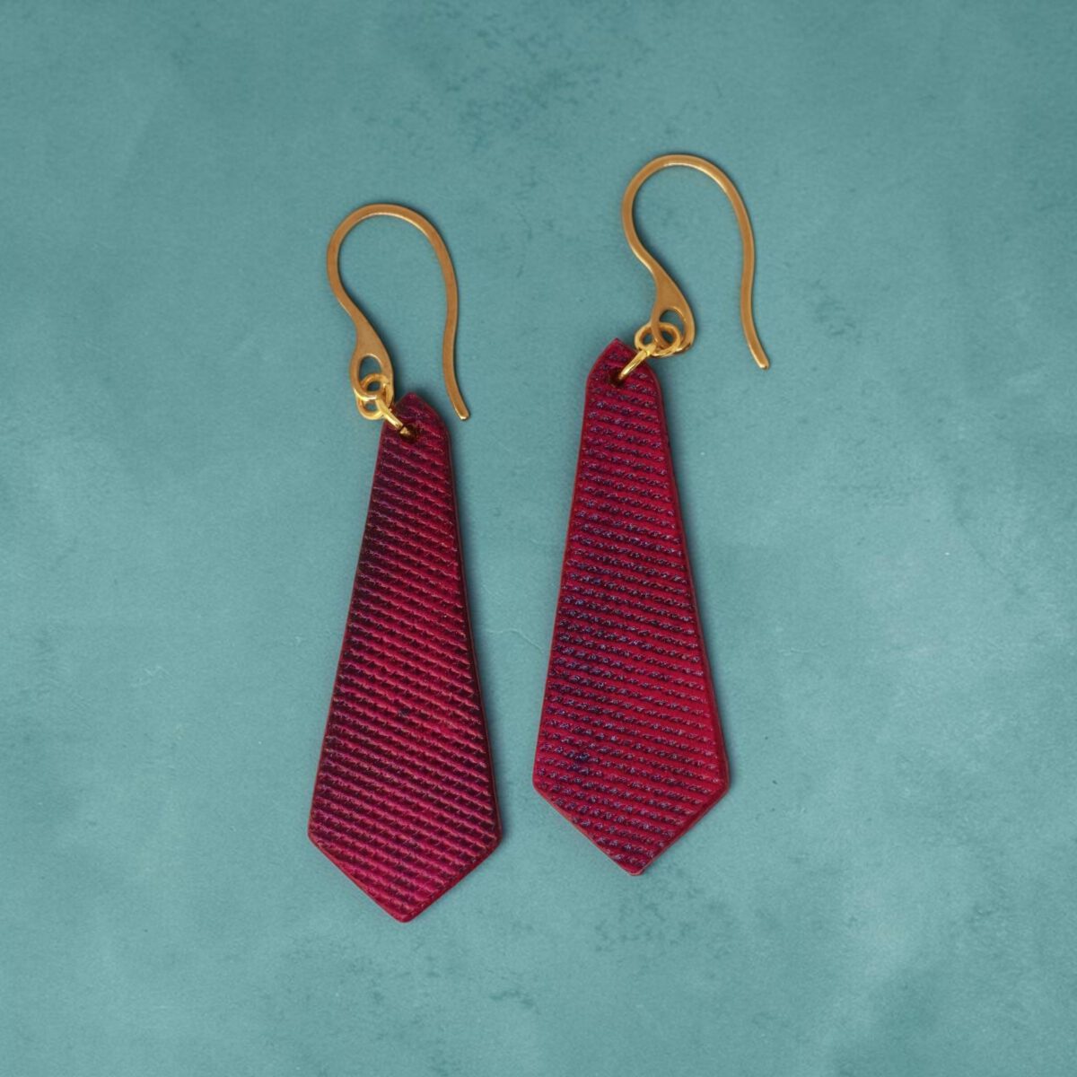 Boucles d'oreilles cravates en cuir teinté fuschia, finition lime vieillie, vues de face, suspendues à des boucles dorées, fond design