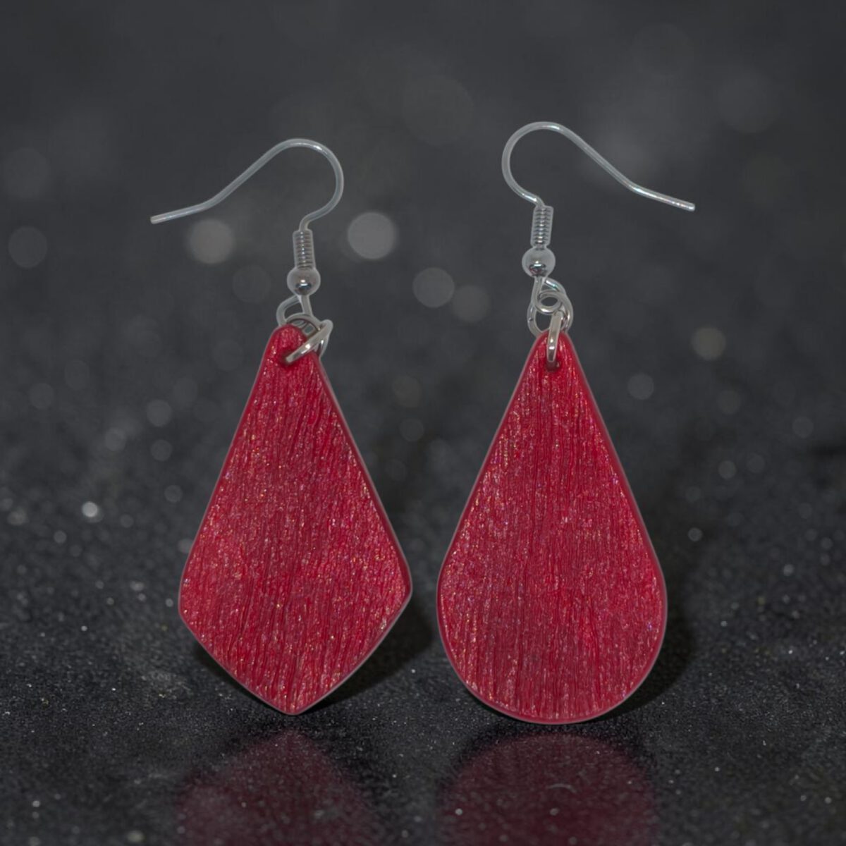 Boucle d'oreille forme larme en cuir teinture rouge, finition griffée, vue de face, suspendue à une boucle argentée, fond noir design