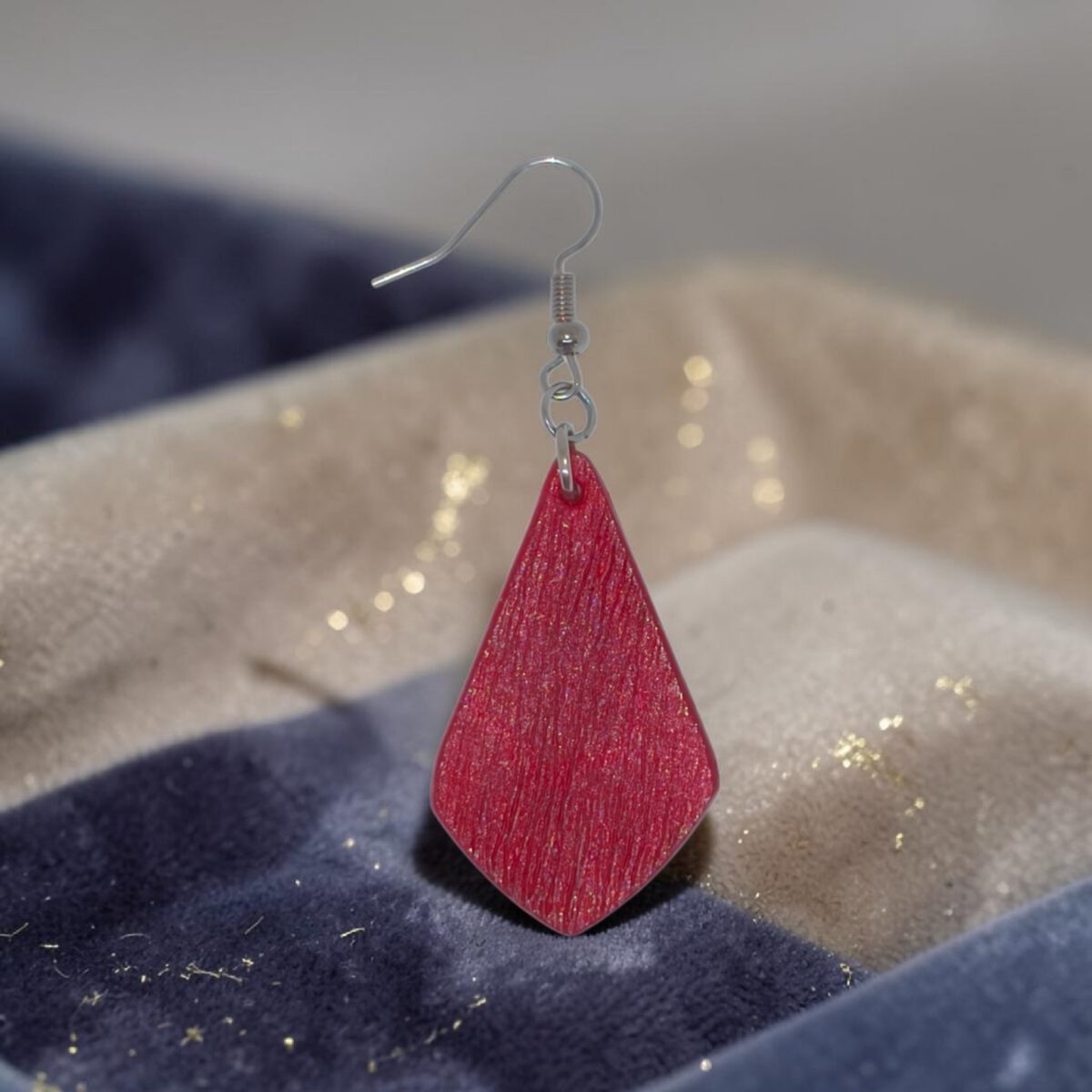 Boucle d'oreille forme larme en cuir teinture rouge, finition griffée, vue de face, suspendue à une boucle argentée, fond fête